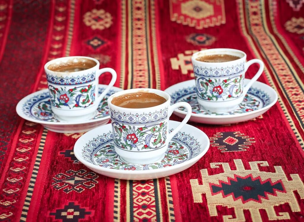 Three cups of traditional Turkish coffee served on a decorative red carpet with highlights of traditional Turkish motifs.